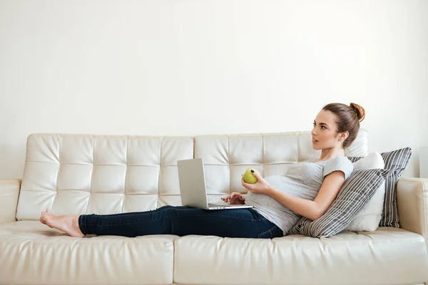 Pensive pregnant young woman thinking and using laptop on sofa — Stock Photo, Image