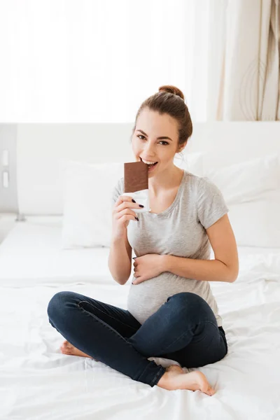 座っているとチョコレート ・ バーを食べて幸せ妊娠中の若い女性 — ストック写真