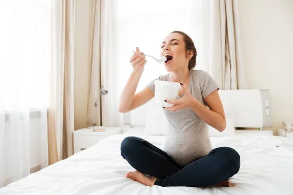 幸福怀孕的年轻女人在床上吃冰淇淋 — 图库照片