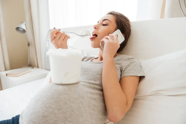Беременная женщина ест мороженое и разговаривает по мобильному телефону — стоковое фото