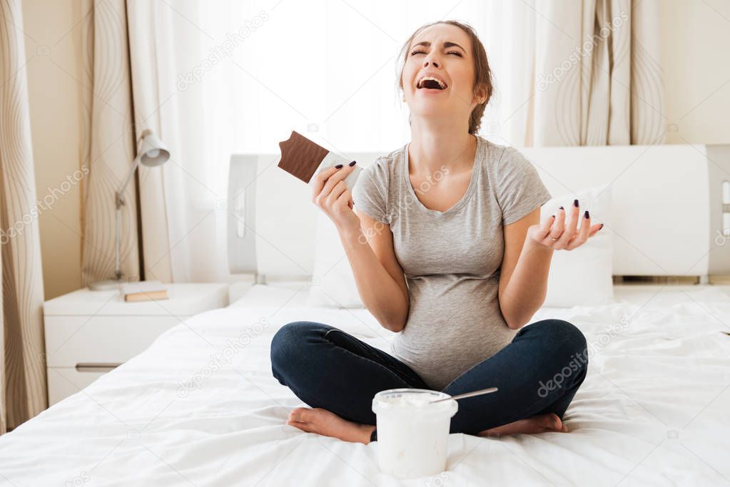 Stressed pregnant woman crying and eating chocolate with ice cream