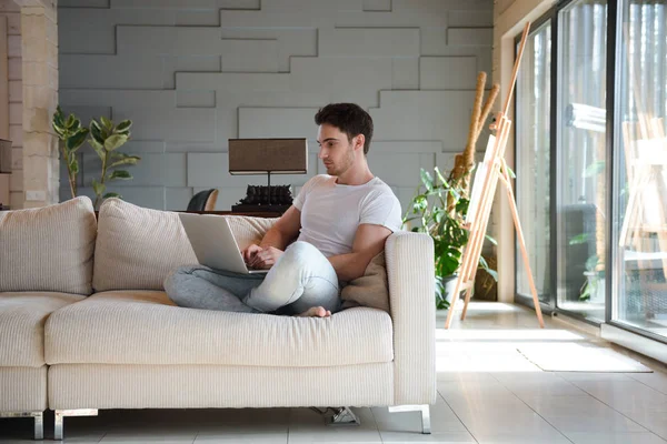Hombre joven usando el ordenador portátil mientras está sentado en la sala de estar —  Fotos de Stock