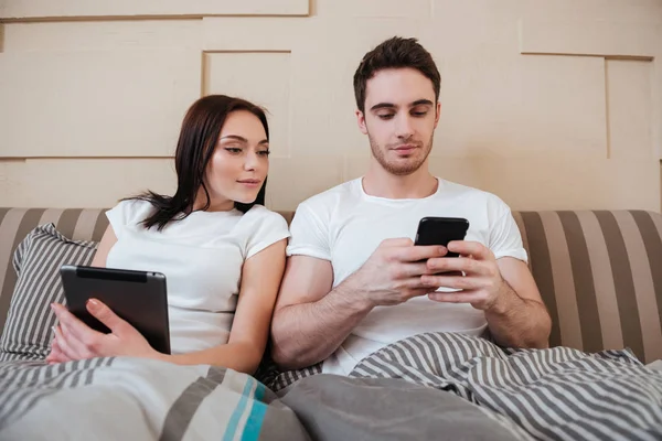 Paar liegt im Bett und benutzt Gadgets — Stockfoto