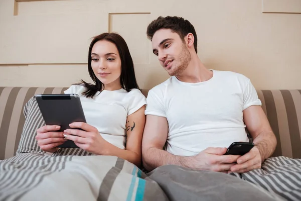 Paar liegt im Bett und benutzt Gadgets — Stockfoto