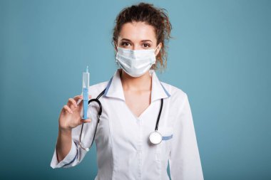 Ayakta ve şırınga tutarak maskeli kadın doktor portresi