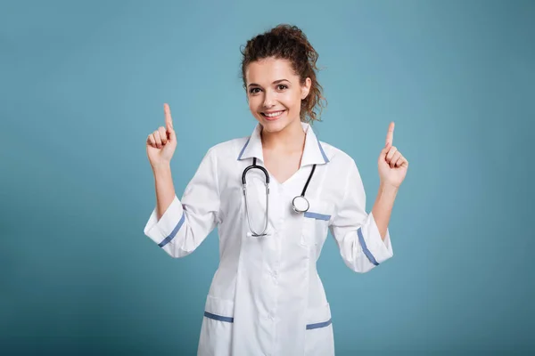 Glad ung sjuksköterska med stetoskop pekar — Stockfoto