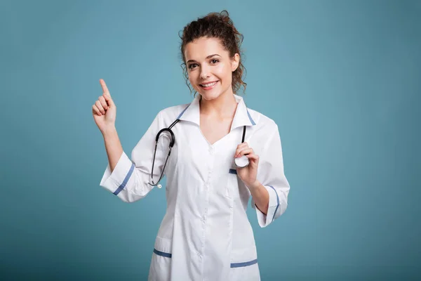 Счастливая молодая медсестра со стетоскопом указывает — стоковое фото