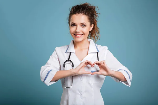 Kvinna läkare med stetoskop visar hjärtat tecken isolerade på blå — Stockfoto