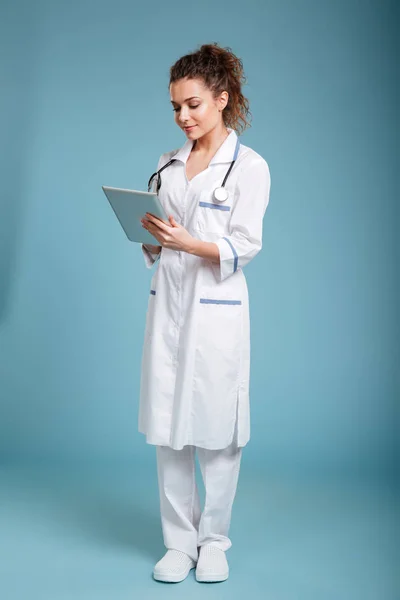 Молодая дружелюбная медсестра стоит и использует компьютерный планшет — стоковое фото