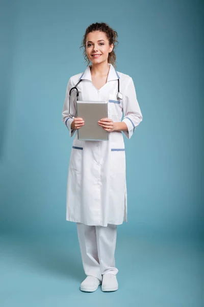 Jeune infirmière amicale debout et utilisant pc comprimé — Photo