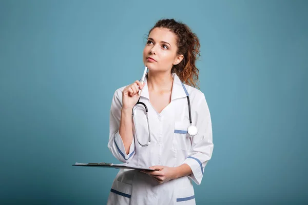 Задумчивая женщина-врач или медсестра держит планшет и смотрит вверх — стоковое фото