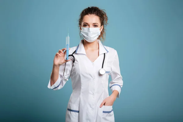 Zdravotní sestra v tvář masku a laboratorní plášti držící injekční stříkačky — Stock fotografie