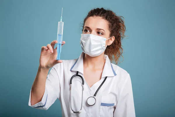 Lady medico guardando siringa in piedi sullo sfondo blu — Foto Stock