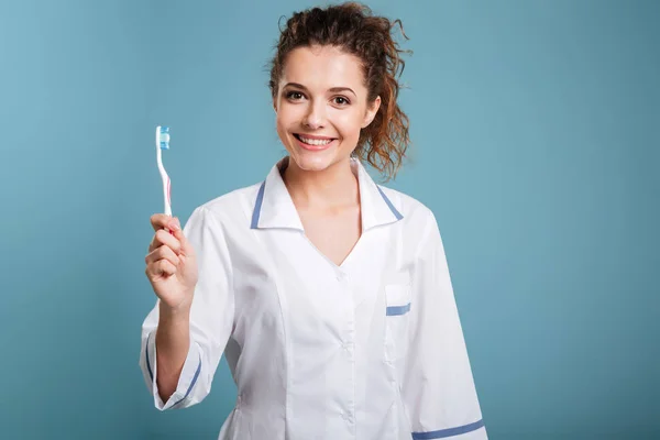 Médica sorridente de casaco branco com estetoscópio e escova de dentes — Fotografia de Stock