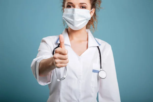 Jistý lékař nebo zdravotní sestra chirurgické masky a ukazuje palec nahoru — Stock fotografie