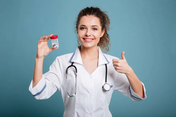 Vrouw verpleegkundige in laboratoriumjas met pillen en duim omhoog geïsoleerd — Stockfoto