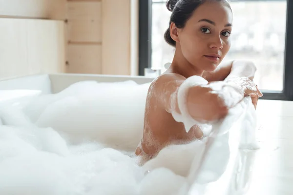 Prachtige charmante jonge vrouw zitten in badkuip met schuim — Stockfoto
