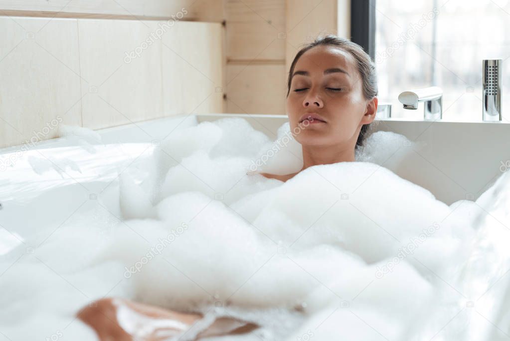 Beautiful young woman with closed eyes resting and relaxing in bathtub