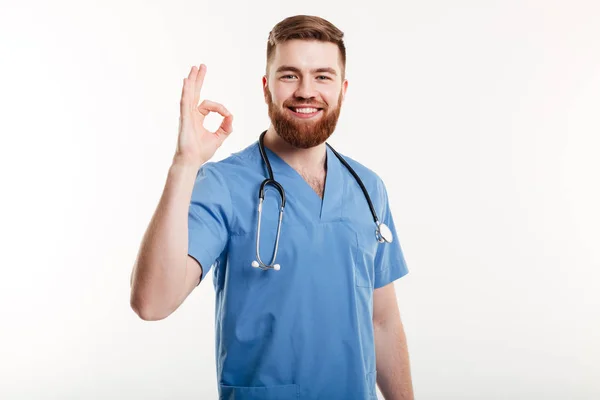 Médico macho amigável feliz com estetoscópio mostrando gesto ok — Fotografia de Stock