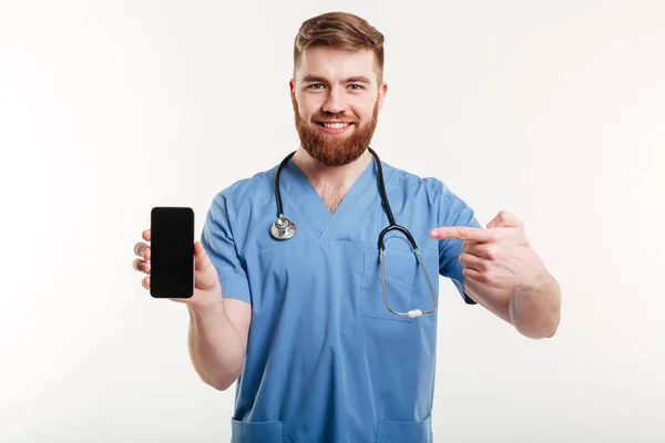 Médico mostrando telefone e sorrindo . — Fotografia de Stock