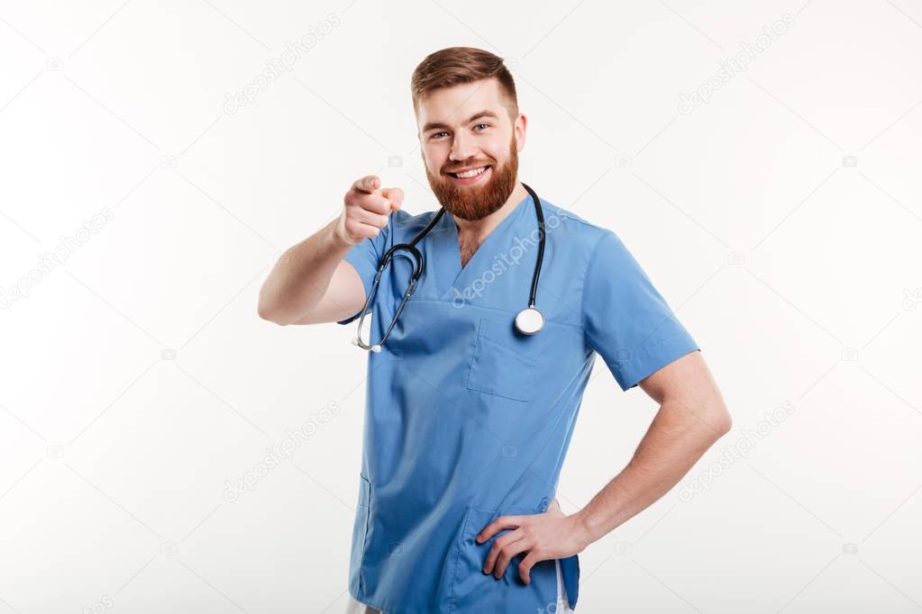 Smiling happy male doctor with stethoscope pointing finger at camera