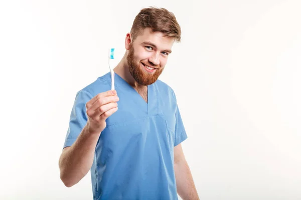 Sorrindo jovem dentista masculino segurando escova de dentes e olhando para a câmera — Fotografia de Stock