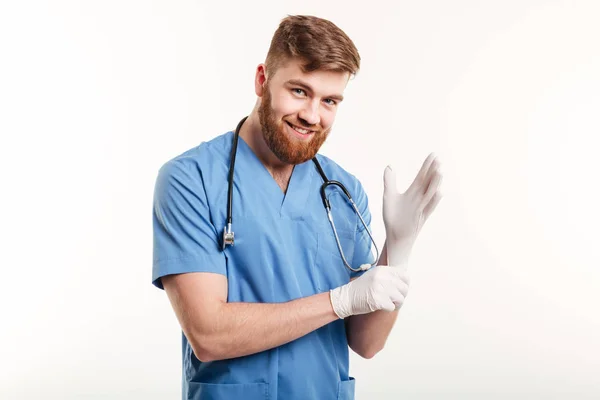 Retrato de um médico amigável sorridente colocando luvas estéreis — Fotografia de Stock