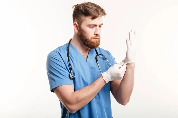 Porträt eines konzentrierten jungen Arztes, der sterile Handschuhe anzieht — Stockfoto