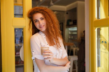 Gülümseyen ayakta ve kahve tutan Kızıl saçlı kadın