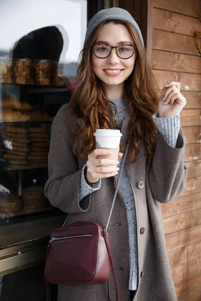 Ayakta ve açık havada kahve içme gülümseyen güzel genç kadın — Stok fotoğraf