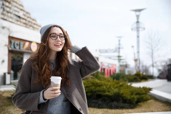 Усміхнена жінка, що йде і п'є, забирає каву на відкритому повітрі — стокове фото