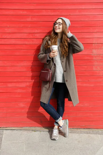 Χαμογελώντας χαλαρή νεαρή γυναίκα στέκεται και πίνοντας take away καφέ — Φωτογραφία Αρχείου