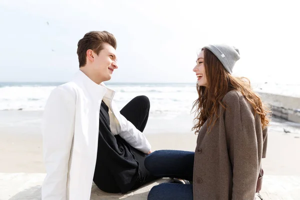 Улыбающаяся пара разговаривает на пляже осенью — стоковое фото
