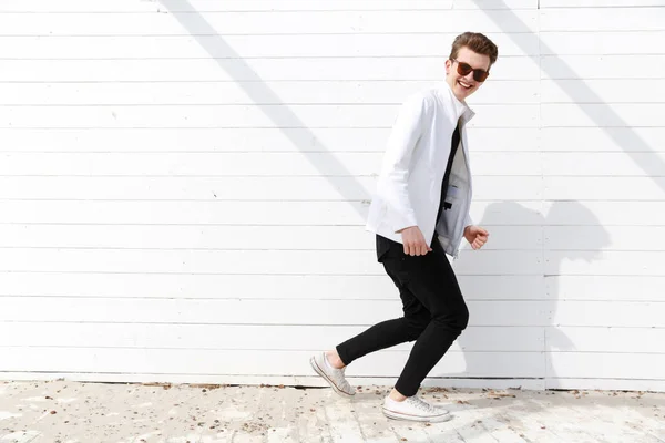 Веселый человек в солнечных очках, бегущий по белой стене — стоковое фото