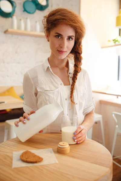 Bella donna dai capelli rossi versando il latte in vetro dalla bottiglia — Foto Stock