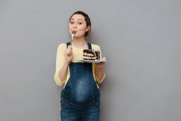 Retrato de una joven embarazada encantada comiendo pastel de chocolate —  Fotos de Stock