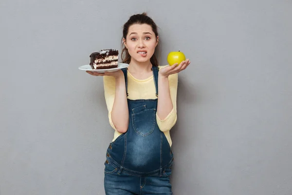 Pregnant lady choosing between sweet cake and apple — Stock Photo, Image