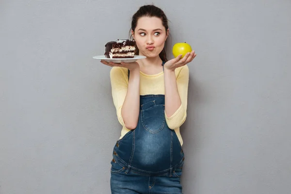 Schwangere hat die Wahl zwischen süßem Kuchen und Apfel. — Stockfoto