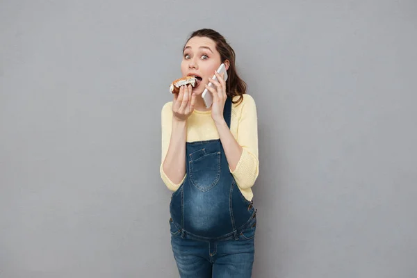 Glada gravida äta éclair och prata via telefon — Stockfoto