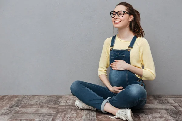 Gravida lycklig kvinna sitter isolerade över grå vägg. — Stockfoto