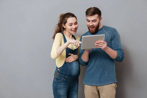 Молода вагітна жінка використовує планшетний комп'ютер зі своїм чоловіком — стокове фото