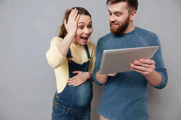 Jonge zwangere vrouw met behulp van tablet pc met haar echtgenoot — Stockfoto