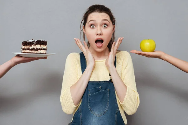 Захваченная беременная женщина выбирает между яблоком и тортом — стоковое фото
