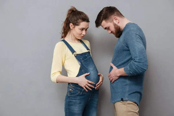 Grávida mulher feliz em pé perto de homem alegre comparar estômagos . — Fotografia de Stock