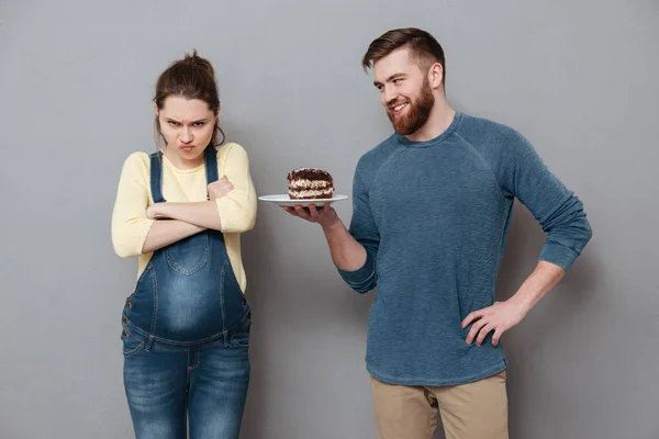 Usmívající se manžel nabízí svou nespokojeni těhotnou manželku čokoládový dort — Stock fotografie