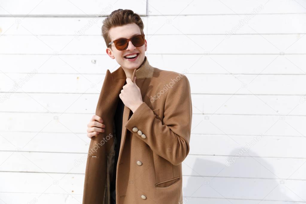 Portrait of smiling attractive young man in coat and sunglasses