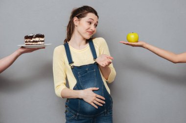 Genç hamile kadın elma ve kremalı pasta arasında seçim yapma karıştı