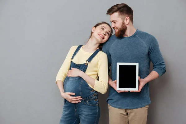 Trevliga par som väntar barn och visar tom tablett datorskärm — Stockfoto