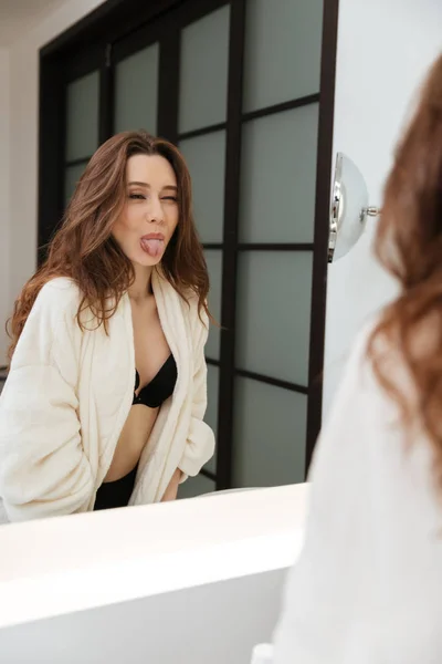 Grappige vrouw spiegel te kijken en het tonen van tong in de badkamer — Stockfoto