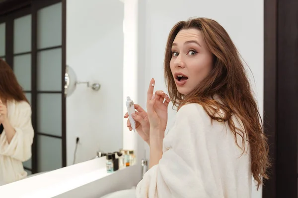 Surprised woman standing and applying cream in bathroom — Stock Photo, Image